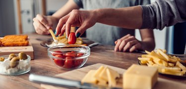 a person's hand taking a cherry tomato from a glass bowl on a wooden table, to represent eating too many tomatoes