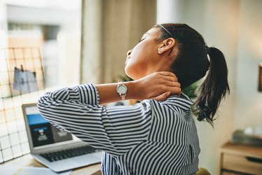 back view of a person with a brown ponytail wearing a striped shirt and holding their stiff neck