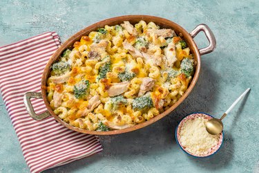 Baked broccoli and chicken casserole in a baking dish on blue marble background beside pamesan cheese