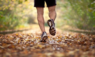 a close up of a runner's lower legs on a leafy trail