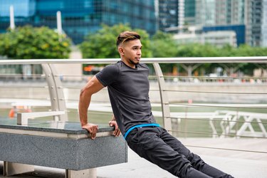 man doing triceps dips outdoors on a park bench