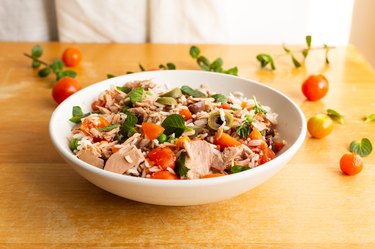 Salad of rice, canned light tuna, tomatoes, olives and aromatic herbs. on wooden table