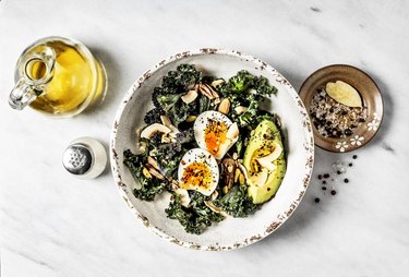 Bowl of kale salad with boiled eggs and avocado on white background