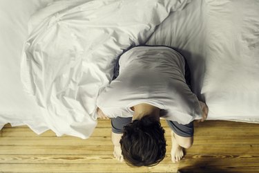 Man sitting on edge of bed holding head because he has pain during sex