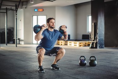 fit person with short hair and a beard doing a double kettlebell squat in the gym as part of the iron cardio workout