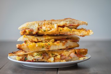 a stack of grilled egg, cheese, ham and tomato sandwiches on a white plate as an example of a leftover ham recipe