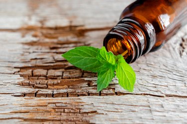 a small brown glass bottle containing a fresh peppermint leaf lying on a wooden table