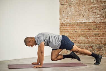 Person wearing gray T-shirt and blue shorts doing mountain climber exercise on mat.