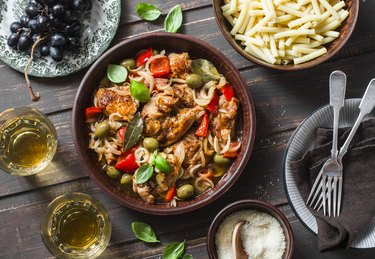 Lunch table. Roasted chicken with olives and sweet peppers, paste, white wine on dark background, top view. Comfort simple food