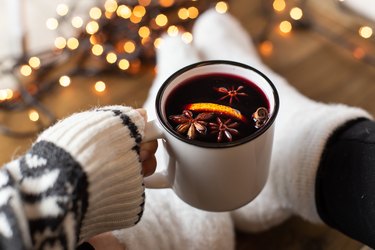 Person holding white mug of mulled wine made in an Instant Pot garnished with star anise cinnamon and orange peels.