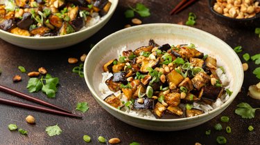 a bowl of an Asian-inspired eggplant dish with rice, peanuts and spring onion next to a pair of chopsticks as an example of food that may be made with added MSG