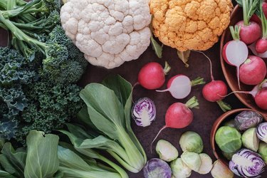 an overhead photo of colorful cruciferous vegetables, including cauliflower, broccoli, Brussels sprouts, radish, kale and bok choy