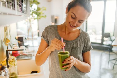 Woman stirring green smoothie in kitchen