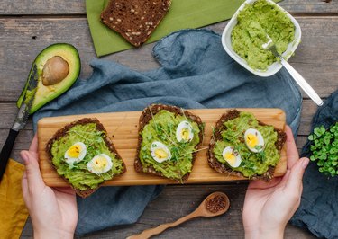 hands holding homemade sandwiches with avocado, eggs and radish sprouts