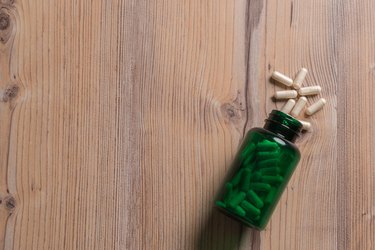 Heap of white Glucosamine capsules in green bottle on wood