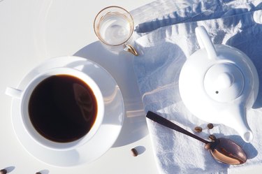 cup of black coffee on white plate and teapot