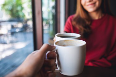 Two people clinking coffee mugs together in cafe after using coffee for hair growth before and after