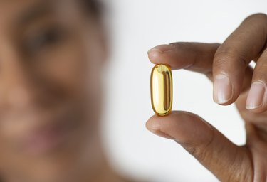 woman holding an omega-3 fish oil supplement capsule between her fingers.