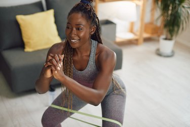 Person in living room doing a squat with a mini resistance band to demonstrate a 20-minute mini band workout.