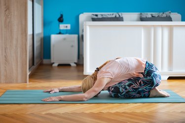 Person doing child's pose on blue yoga mat beside bed before going to sleep.