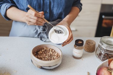 Hands of a Woman Adding high-protein yogurt to Rolled Oats, Healthy Breakfast Concept