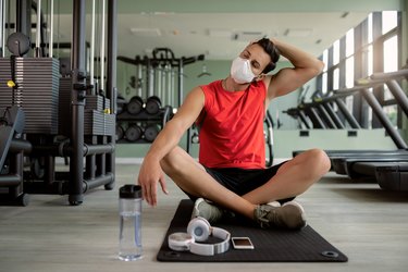 Male athlete with face mask warming up and stretching his neck in a gum.