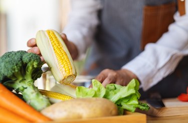 A woman chef holding and picking a fresh corn from a vegetables tray