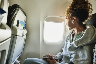 Person wearing gray sweatshirt looking out window of airplane.