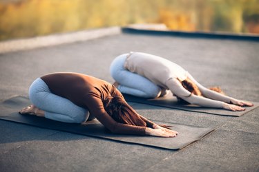 youg women doing child's pose on black yoga mats outside