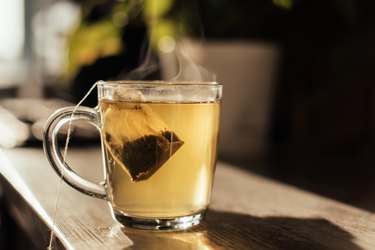 glass mug of hot water with tea bag steeping on wooden counter