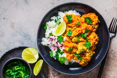 Dutch oven lentil curry served with rice and a wedge of lime on tabletop.