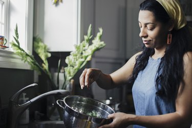 Woman washing food in colander standing at kitchen sink