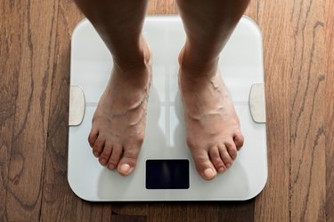 Top down view of feet standing on a white digital bathroom scale on a wooden floor