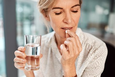 an older adult takes one of the best multivitamins for women over 60 with a glass of water in hand