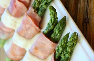 a close up of asparagus spears wrapped in ham on a white platter