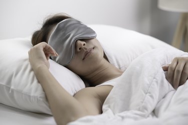 Person sleeping peacefully wearing a gray eyemask under one of the best cooling comforter for hot sleepers