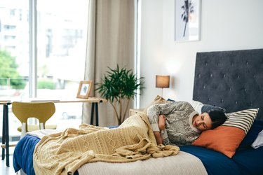 a person lying in bed under a yellow blanket after waking up nauseous