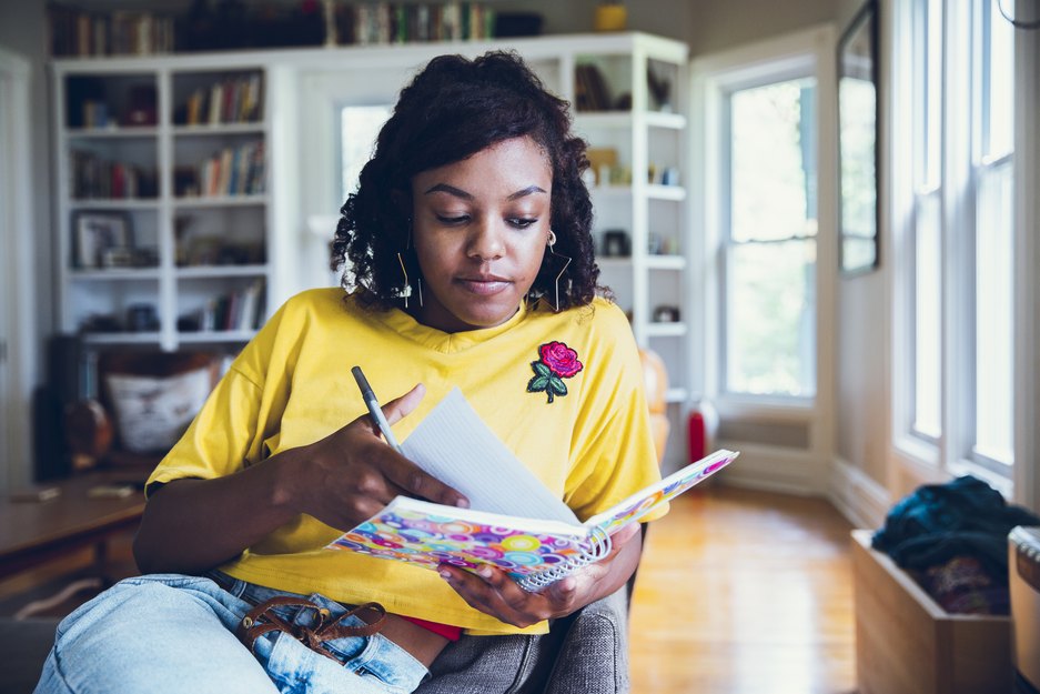 Young woman writing in notebook about healthy food resolutions she wants to make this new years