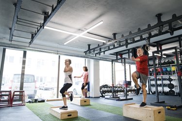 Group of three older adults doing box step-ups in gym as an example of a plyometric exercise.