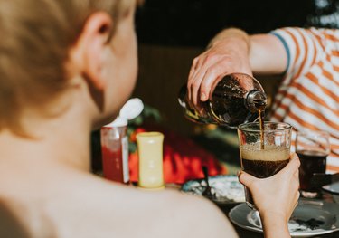 An adult filling a child's glass with brown soda