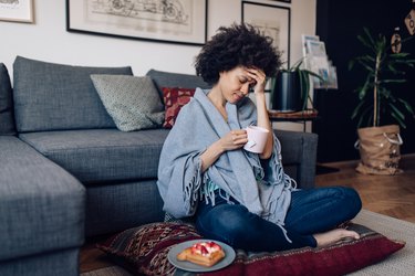 adult woman sitting at home wrapped in blanket and drinking tea for anxiety