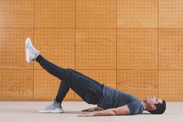 Person doing a single--leg glute bridge against an orange wall