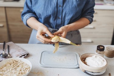 Hands of a Woman Peeling a Banana for Greek Yogurt, two posbiotic foods