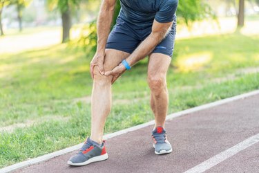 older adult wearing shorts and tennis shoes on a track holds knees weakening with age