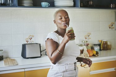 Young person enjoying a protein smoothie in a kitchen with yellow cabinets