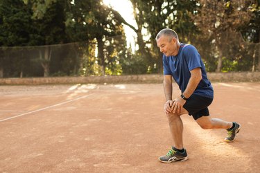 Older adult warming up and exercising on tennis court.