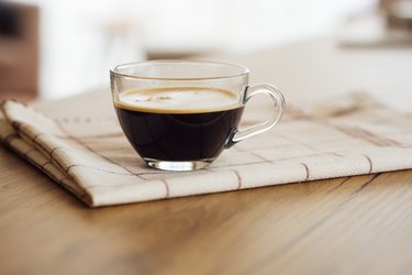 Clear espresso cup of black coffee on a napkin on wooden table, one of the best drinks for constipation