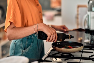 Woman in kitchen pouring oil into pan on stove