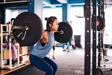 Person in the gym performing a barbell back squat as part of a beginner barbell workout program.