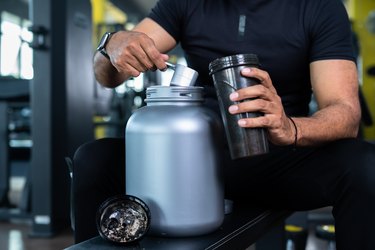 close up shot of bodybuilder scooping best muscle-building supplement powder into protein shaker